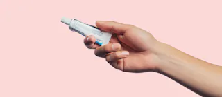 A hand holding a tube of tretinoin cream against a plain pink background.