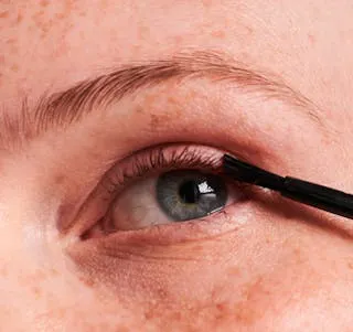 Close up image of women's eye applying eyelash growth serum to lashes