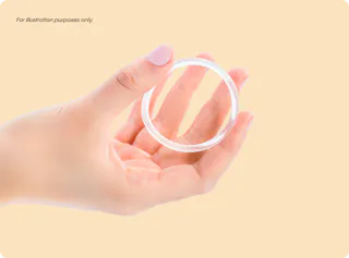 A hand holding a transparent ring-shaped object against a light beige background. Text in the top left corner reads 