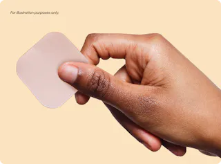 A hand holds a translucent adhesive patch against a beige background.