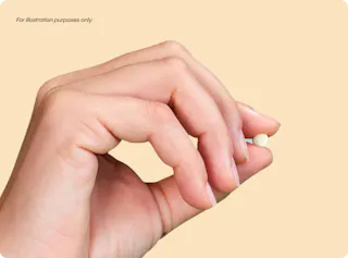 A hand holding a small, round, white object between the thumb and index finger against a plain background.