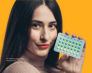 A person holding a blister pack of birth control pills against a bright yellow background.