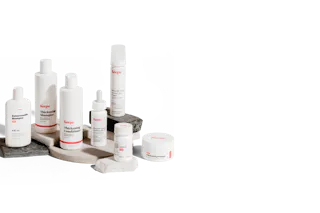 An array of Keeps hair care products, including shampoo, conditioner, and styling cream, displayed on circular stone platforms against a plain background.