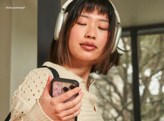A person wearing headphones and a sweater looks at their phone screen, standing indoors.