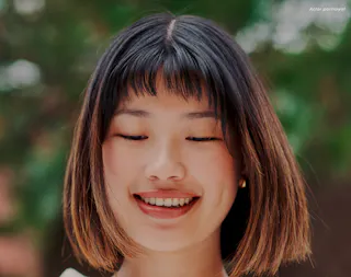 Portrait of a person with short hair and closed eyes, smiling gently against a blurred green background.