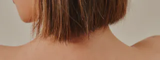 A person's back and shoulders are shown, with short, straight brown hair, hinting at a skincare routine possibly incorporating Tretinoin Cream for enhanced clarity and brightness.