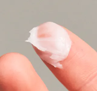 Close-up of a finger with a dollop of pinkish tretinoin cream on the fingertip stands out against a neutral background.