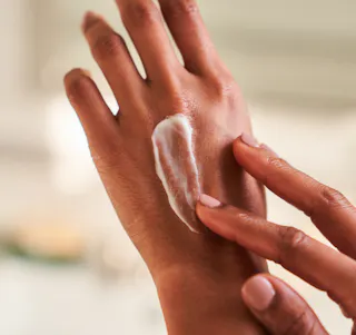 Close-up of a person gently applying tretinoin cream to the back of their hand using their other hand, with a softly blurred background.