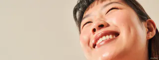 A person smiling brightly, looking upwards, their eyes reflecting joy. The close-up captures their clear complexion, perhaps thanks to Tretinoin Cream. The background is a light, neutral color.