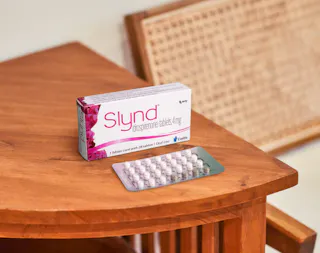 A box of Slynd drospirenone tablets and a blister pack with pills are placed on a wooden table.
