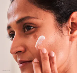 A person gently applies a dab of Tretinoin cream on their cheek with their fingers.