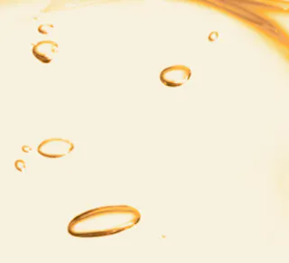A close-up of golden oil droplets, reminiscent of the rich texture of tretinoin cream, suspended in a pale liquid background.