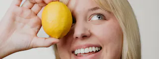 Person holding a lemon up to their left eye, smiling.