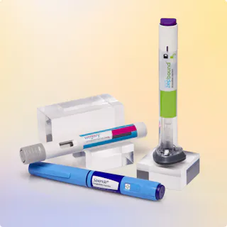 Three different injectable medication pens are displayed upright and lying down on clear rectangular stands against a gradient background.