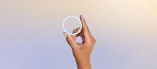 A hand holds up a white, flexible ring-shaped object against a soft gradient background.